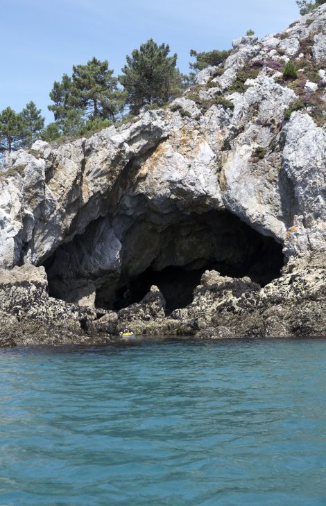 Hochformatige Naturszenerie einer Limestone-Seehöhle mit blauem Meer und Himmel, der vom Meer aus in Richtung Küste blickt - mit Seekajak, um die enorme Größe der Höhle zu zeigen.